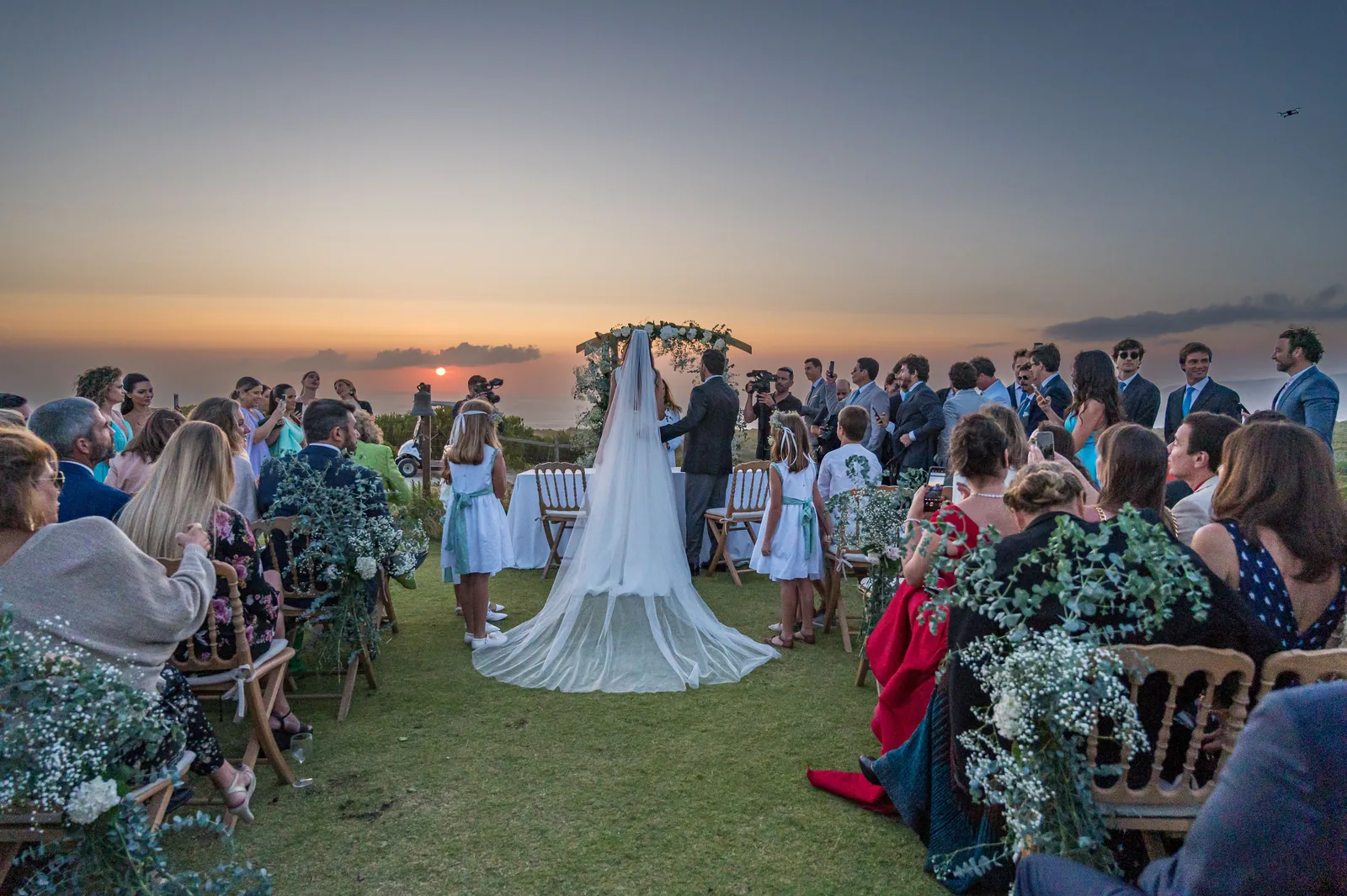 Cerimónia de casamento ao pôr do sol, convidados virados para os noivos